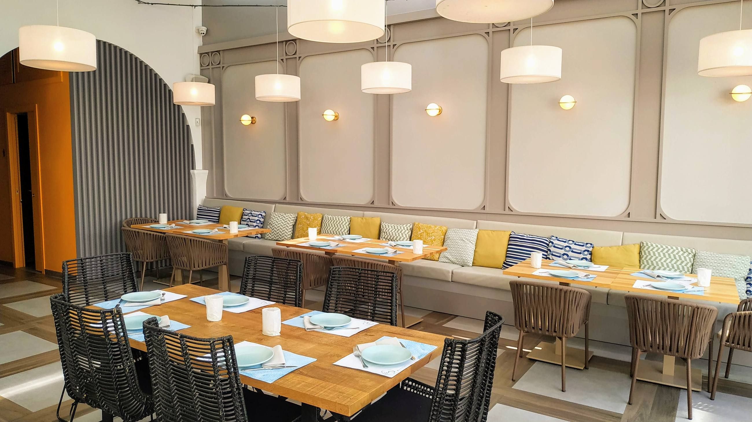 Comedor con banco corrido tapizado y cojines de colores junto a mesas de madera