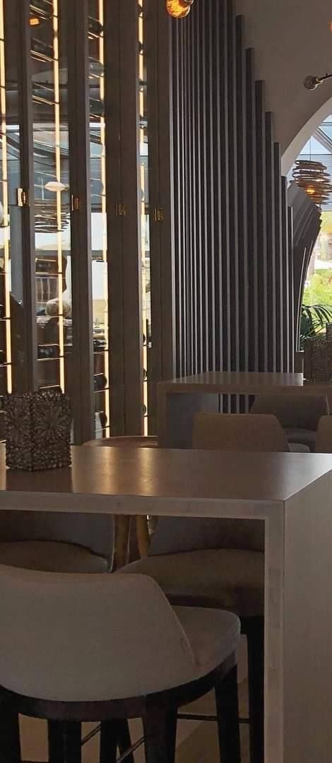 Pasillo de un restaurante con columna de listones curvos y mesas altas de madera