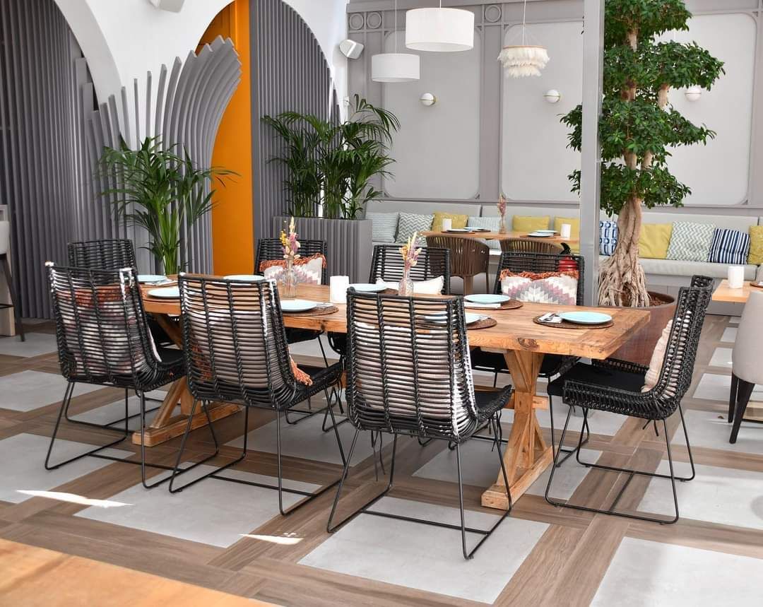 Mesa de madera maciza con sillas de fibra sintética negra en un comedor con plantas