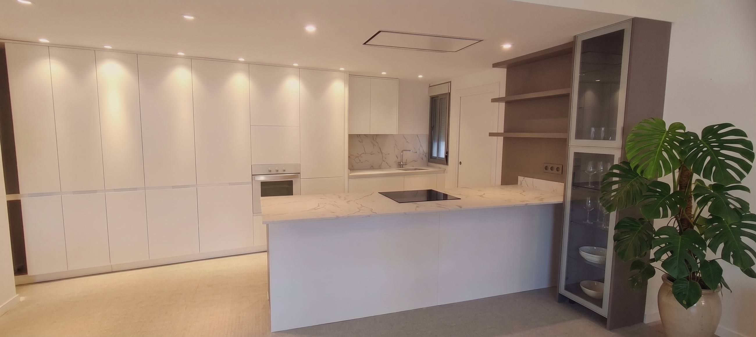 Cocina moderna con isla de mármol, mueble vitrina y bancada corrida de armarios blancos