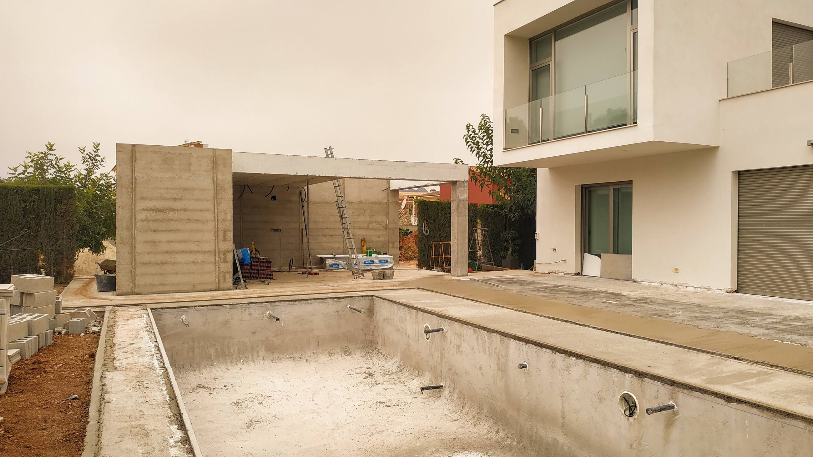 Piscina en fase de obra bruta, con el vaso de hormigón encofrado, junto a una vivienda moderna