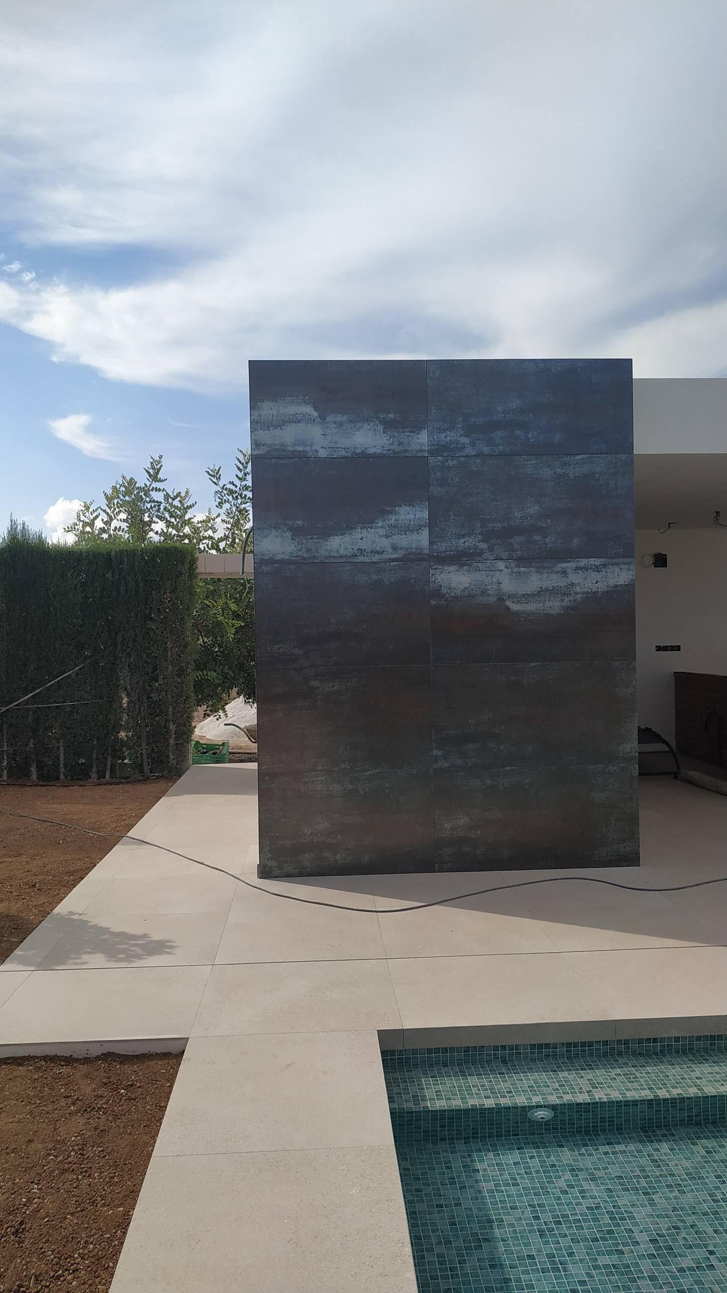 Muro revestido de piedra oscura junto a una piscina en construcción