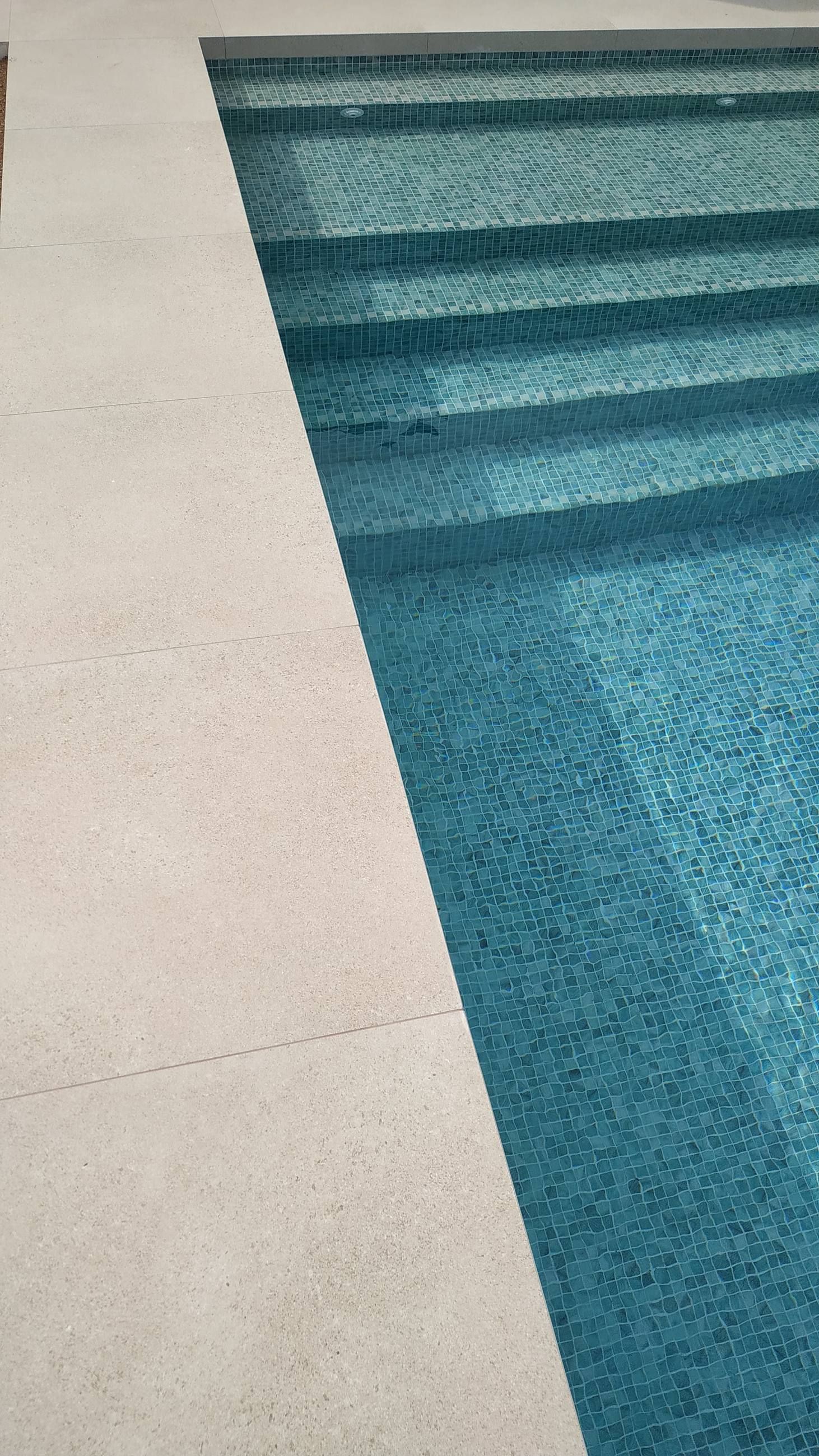 Escalones de piscina revestidos en mosaico de vidrio verde y turquesa